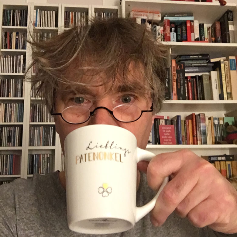 Jens verstrubbelt am Morgen mit Kaffeetasse vor dem Gesicht.